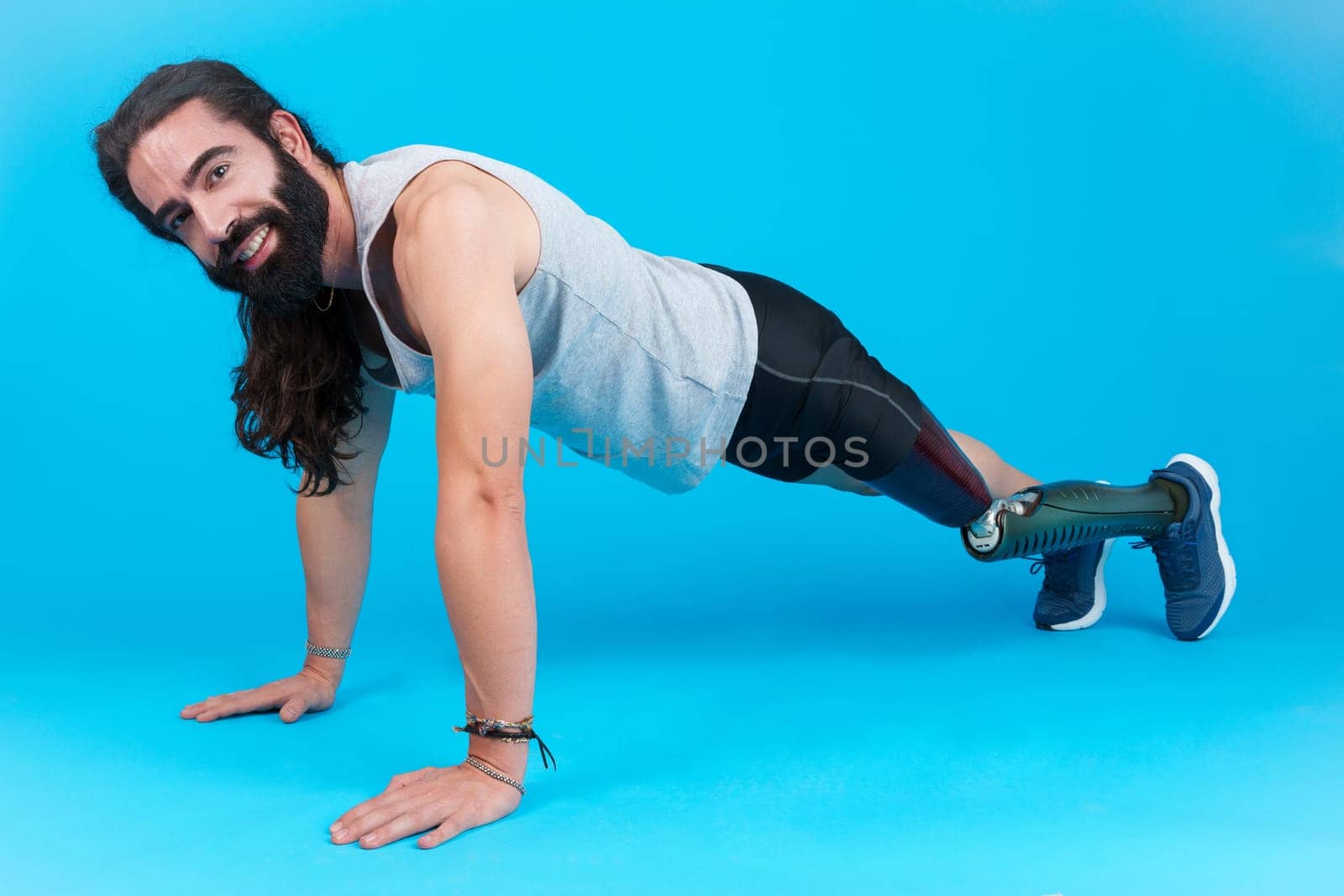 Horizontal studio portrait with blue background of a sportive man with a prosthetic leg doing push-ups on the floor