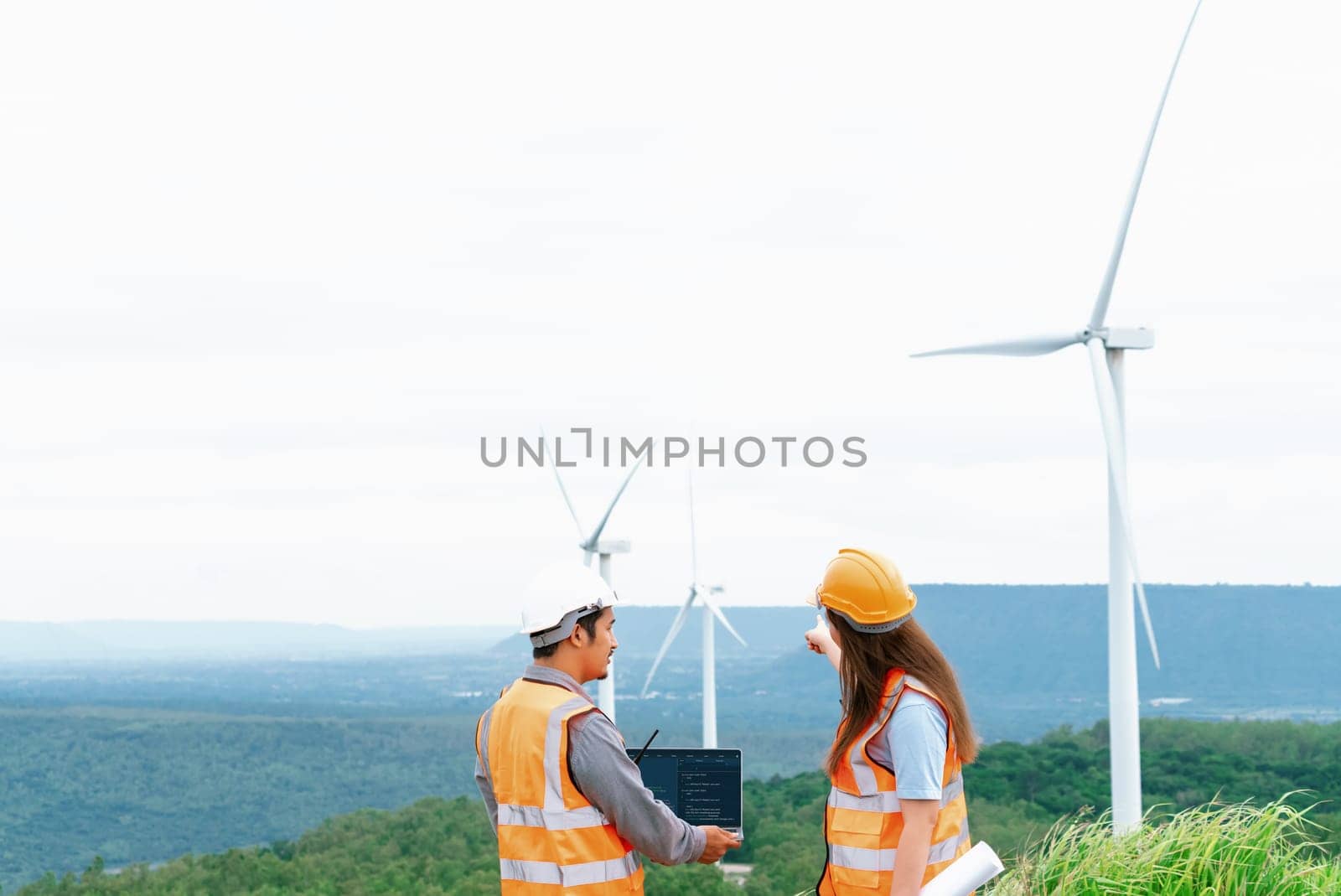 Male and female engineers working on a wind farm atop a hill or mountain in the rural. Progressive ideal for the future production of renewable, sustainable energy.