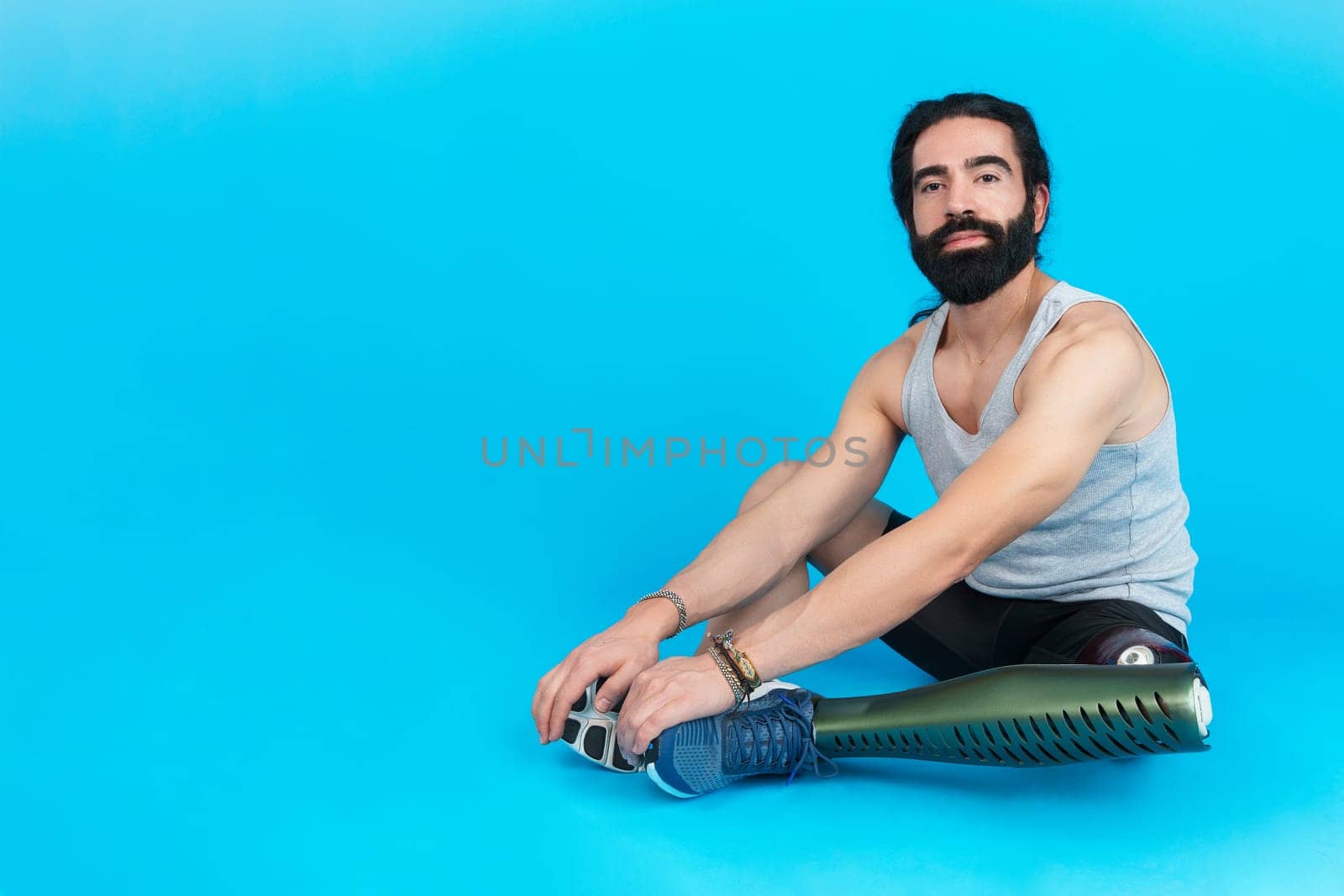 Horizontal studio portrait with blue background of a sportive man with a prosthetic leg sitting on the floor