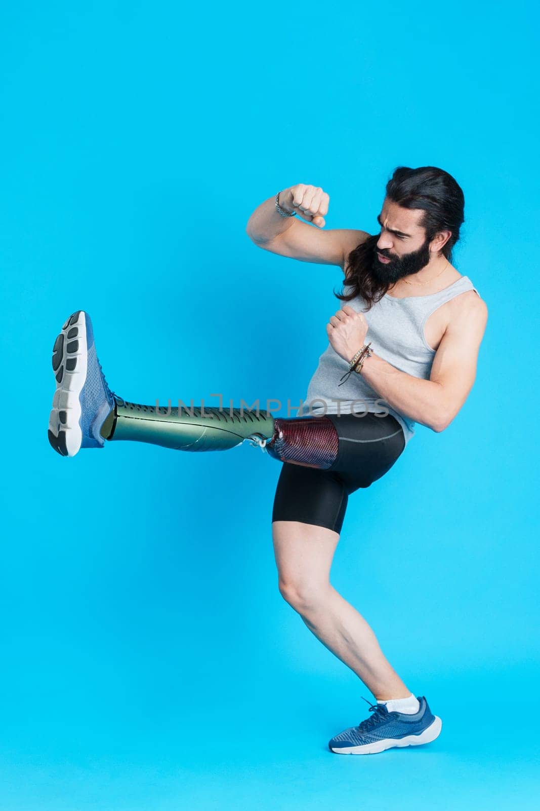 Vertical Studio portrait with blue background of a man with a prosthetic leg kicking and fighting