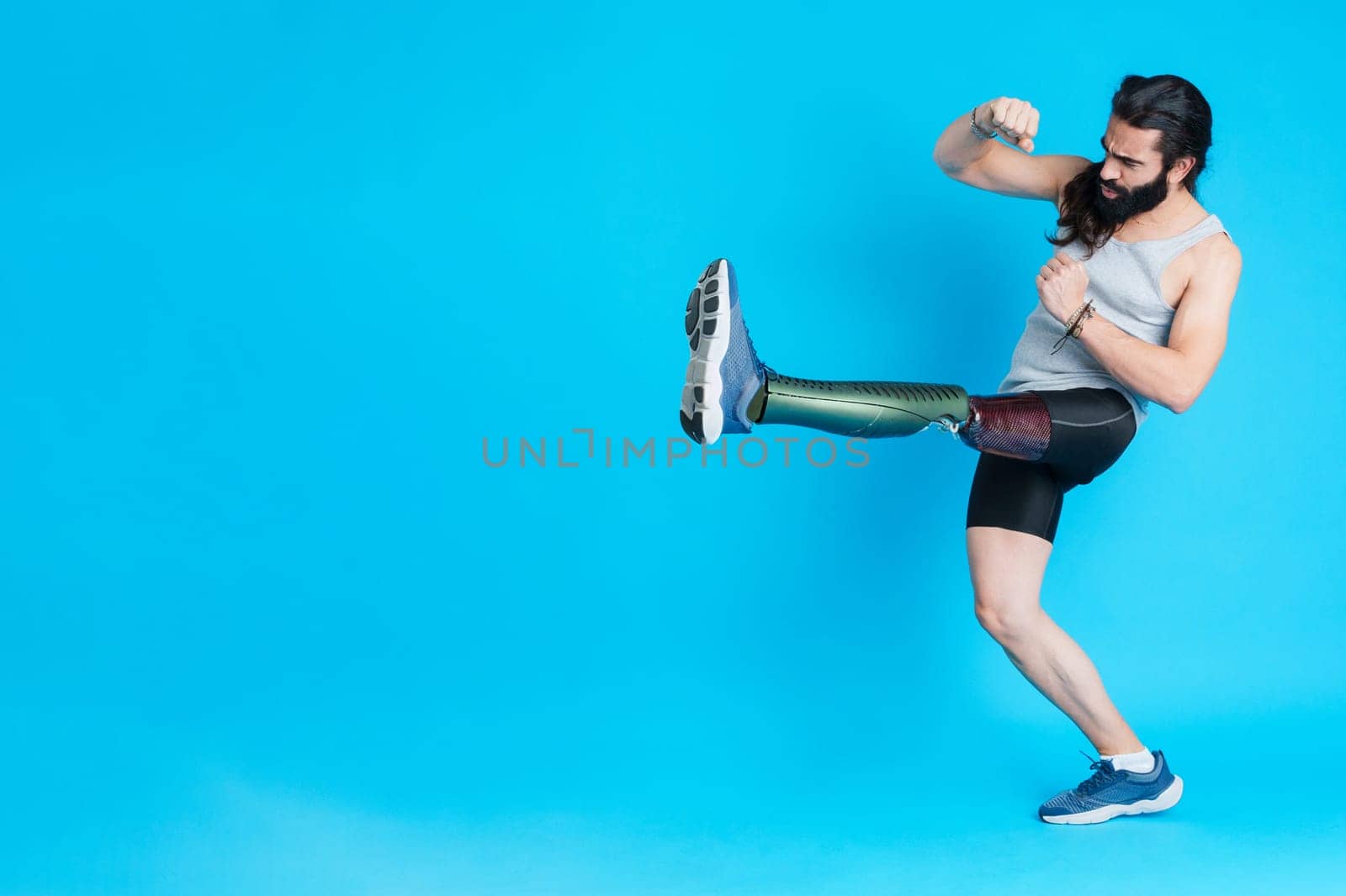 Studio portrait with blue background of a man with a prosthesis on his leg kicking and fighting
