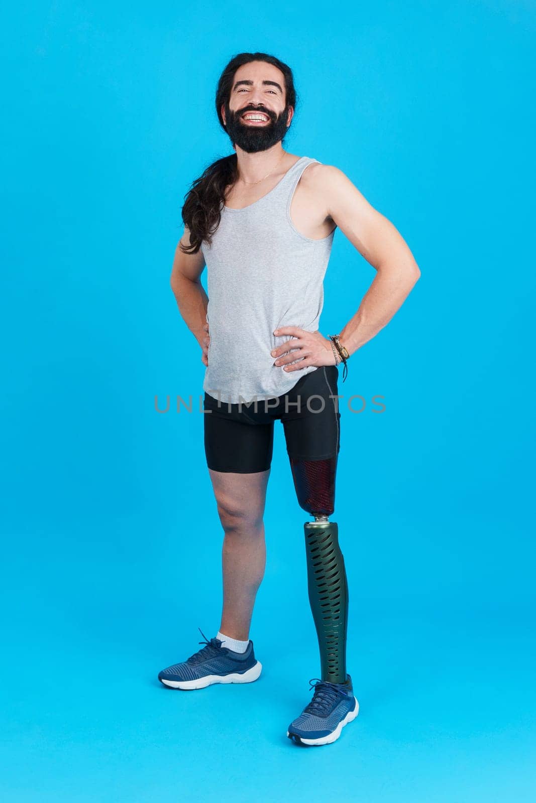 Vertical Studio portrait with blue background of a sportive man standing and smiling with a leg prosthesis