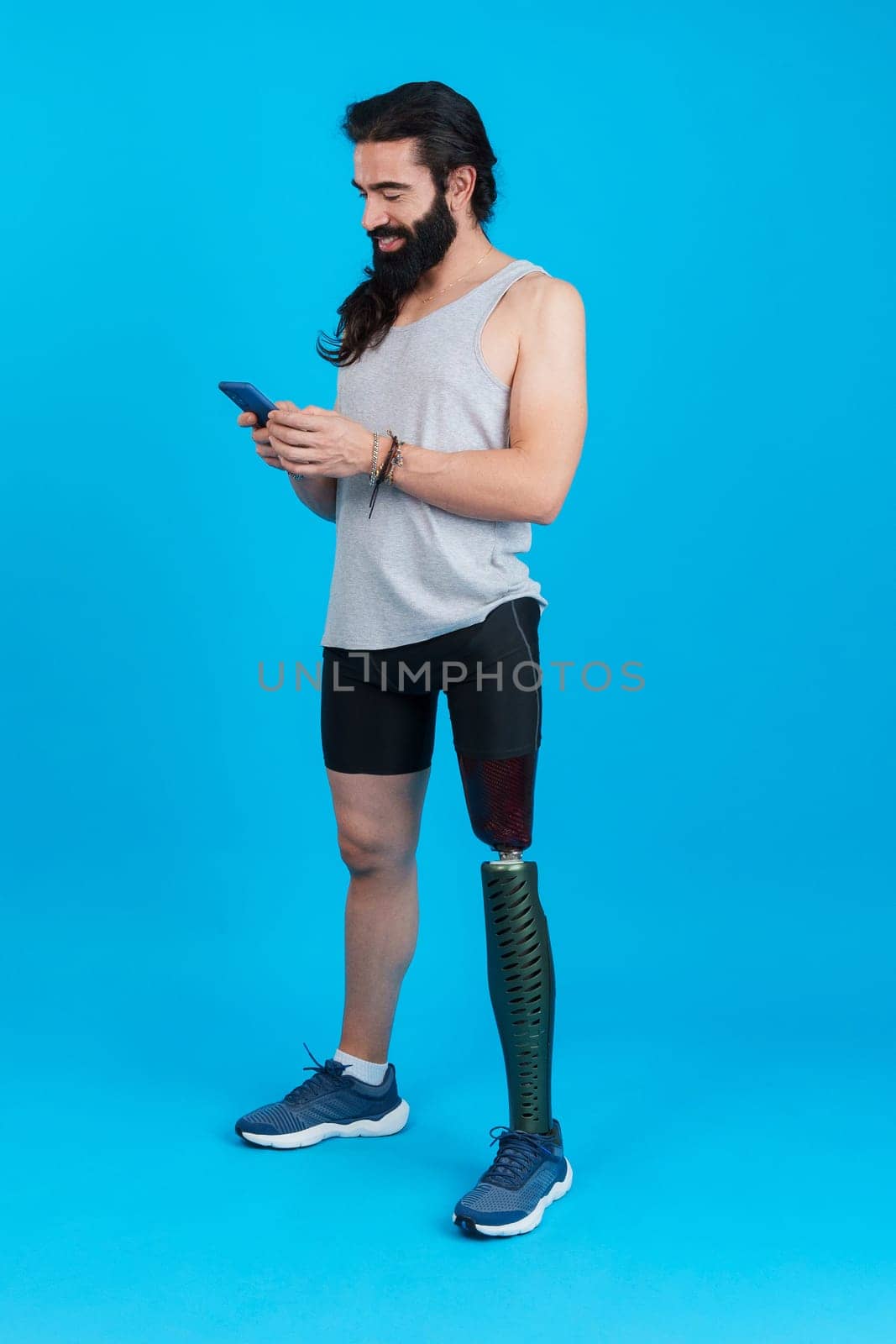 Vertical Studio portrait with blue background of a man with a leg prosthesis using a mobile