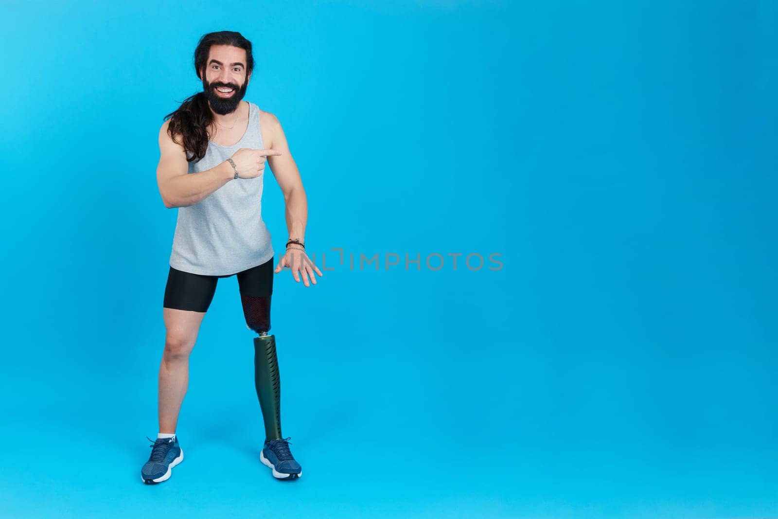 Studio portrait with blue background and copy space of a man with a prosthesis on the leg pointing aside