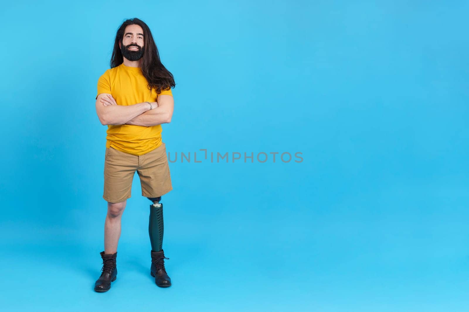 Studio portrait with blue background and copy space of a serious man with prosthesis on the leg standing with arms crossed
