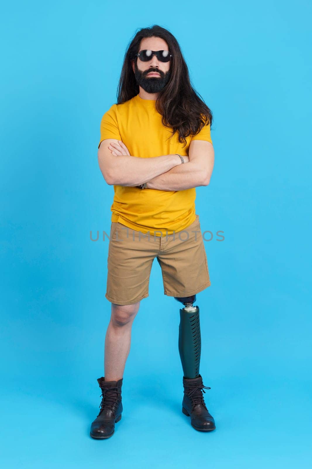 Vertical studio portrait with blue background of a rude man with a leg prosthesis looking at camera with the arms crossed