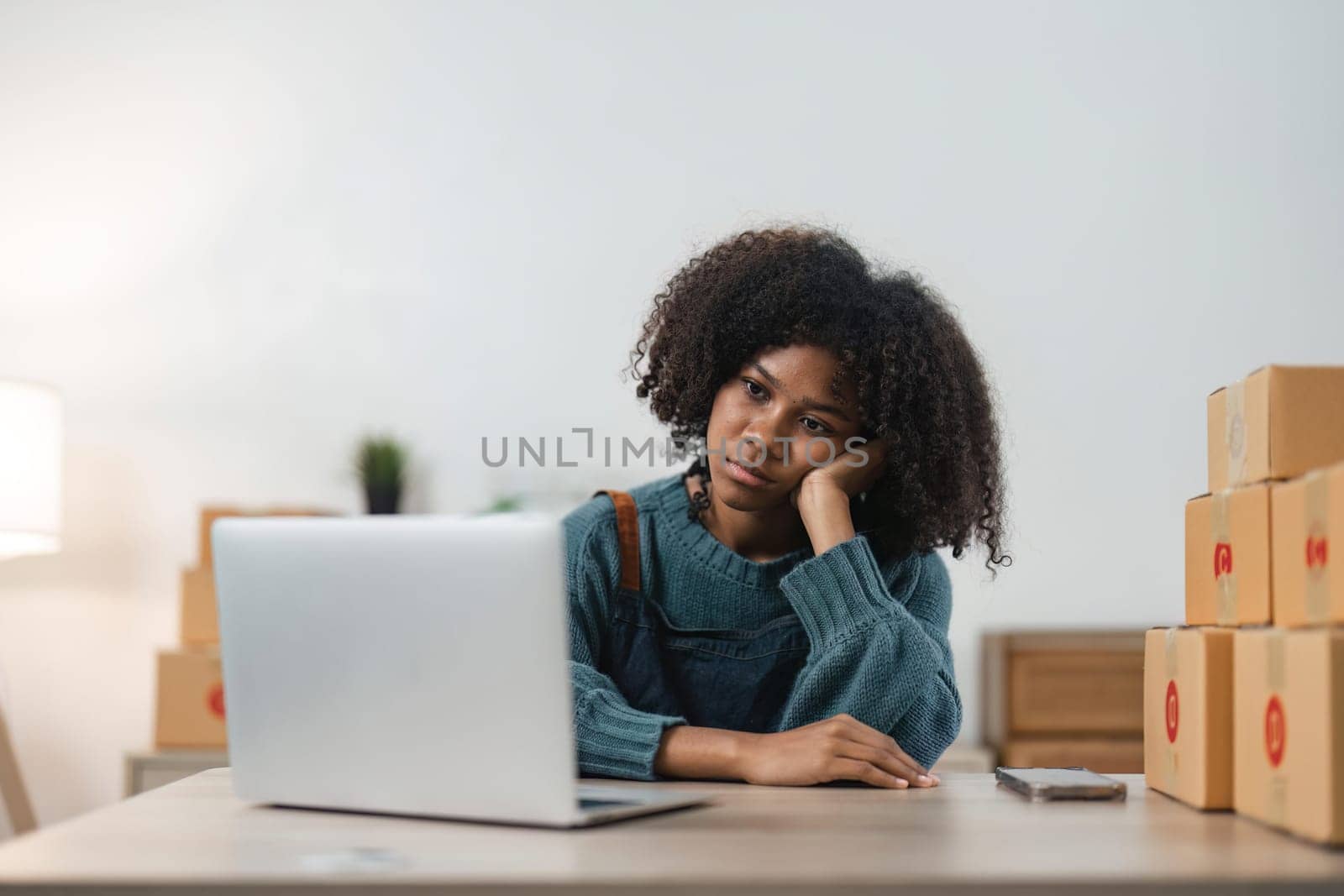 Stressed young entrepreneur African American woman and courier parcel box at home office. Small business owner, online market delivery, lifestyle freelance concept by nateemee