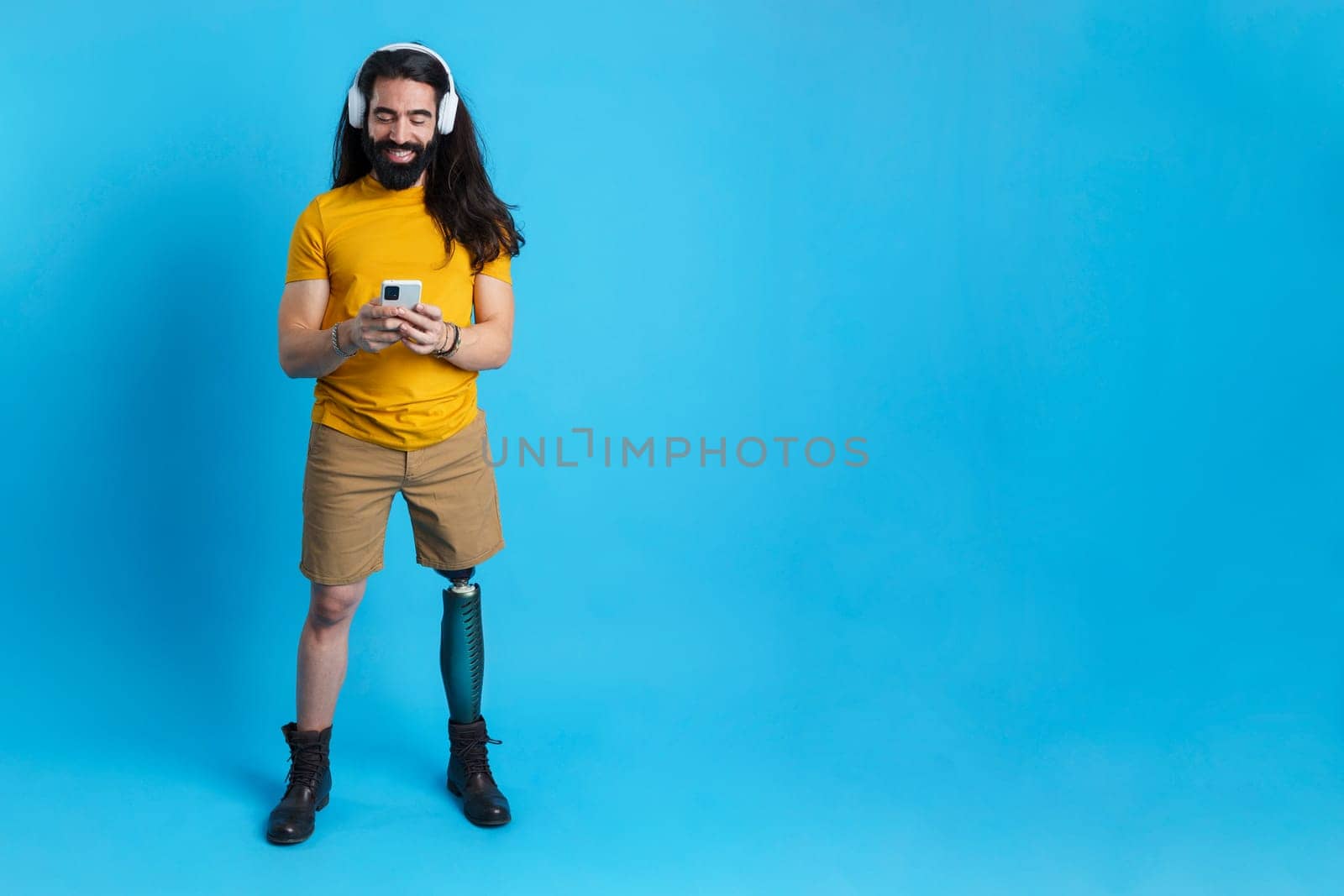 Studio portrait with blue background and copy space of a man with prosthetic leg using the mobile and listening to music