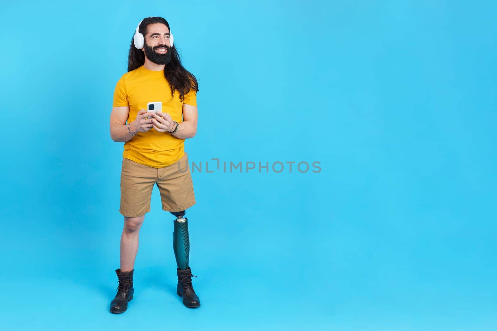 Studio portrait with blue background and copy space of a cool man with prosthetic leg listening to music with the mobile