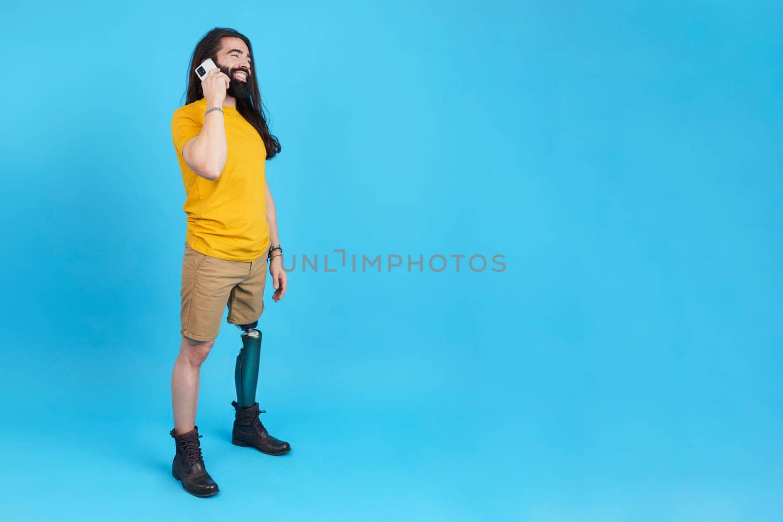 Studio portrait with blue background and copy space of a man with prosthetic leg talking to the mobile phone and smiling
