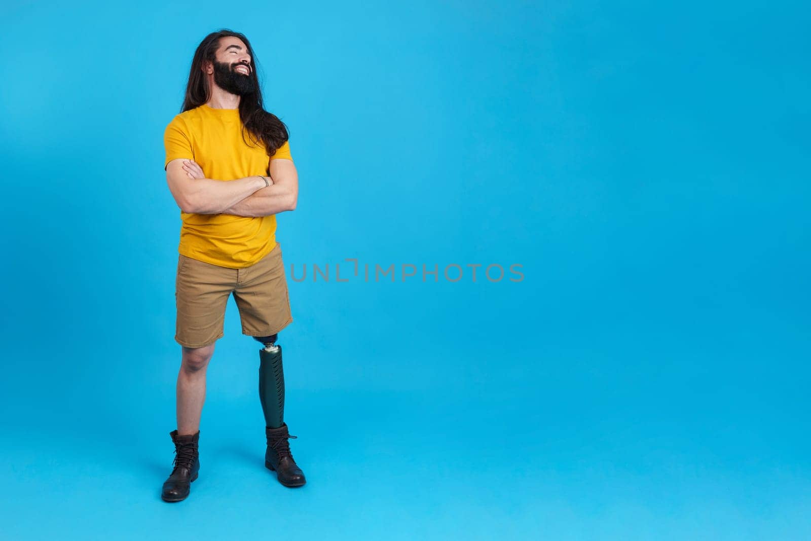 Studio portrait with blue background and copy space of a smiling man with prosthetic leg looking to the copy space aside