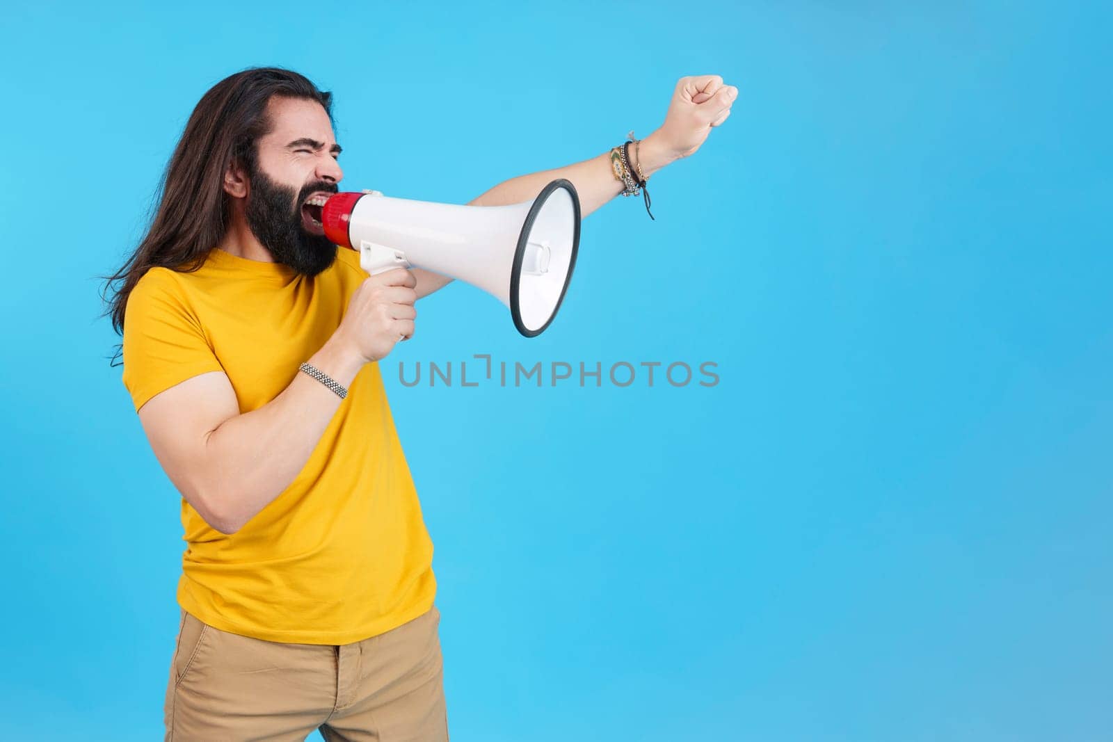 Studio portrait with blue background and copy space of a man protesting while shouting with a loudspeaker
