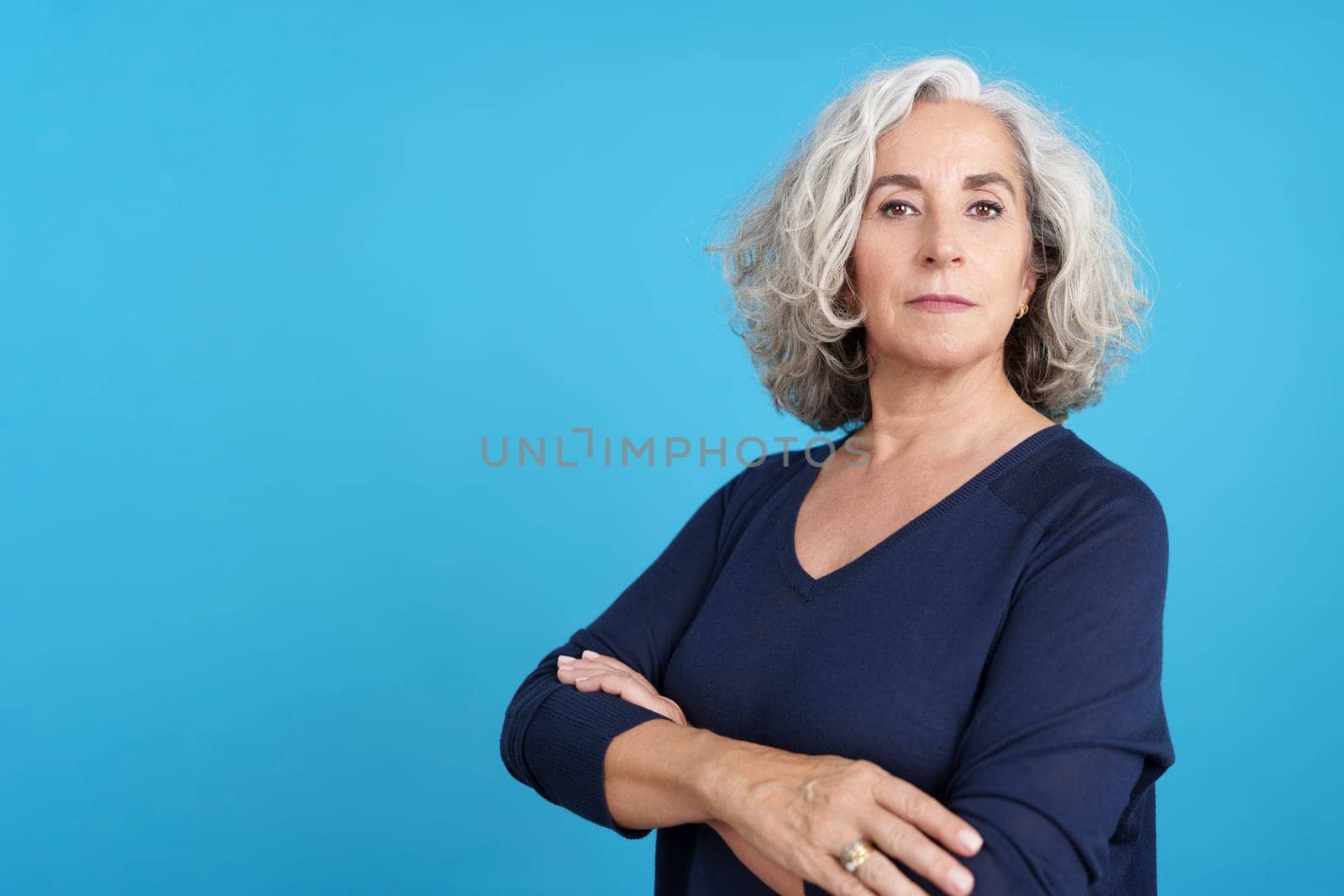 Studio portrait with blue background of a mature woman looking at camera with arms crossed