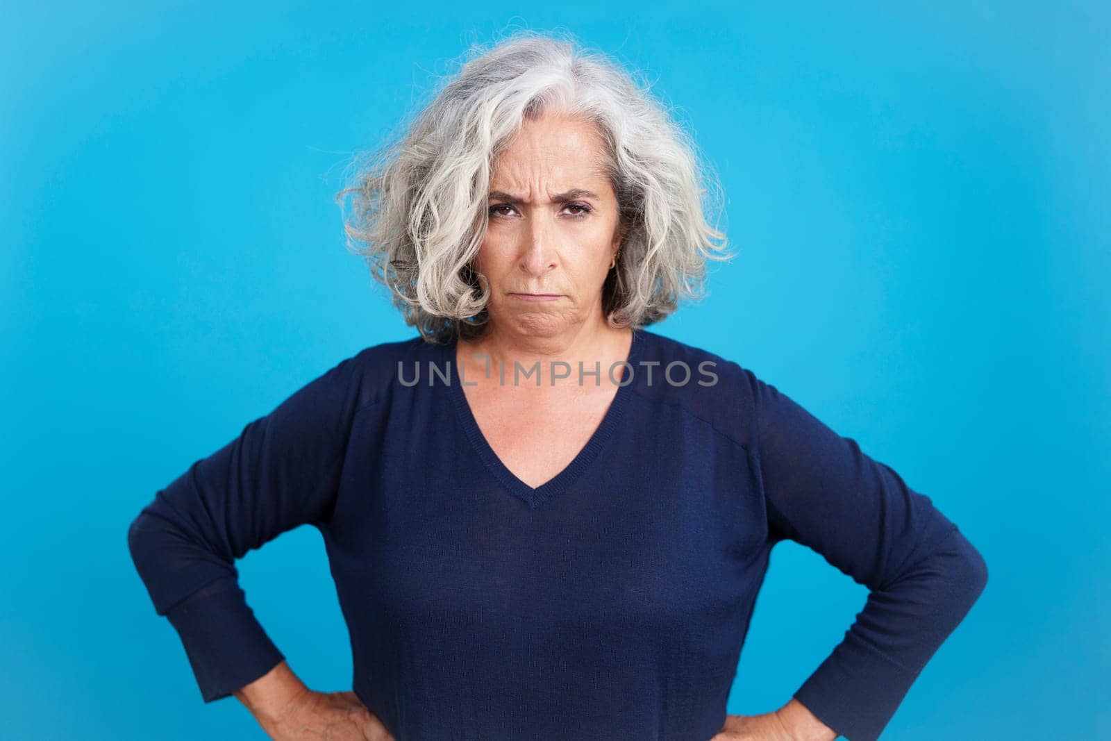 Studio portrait with blue background of a mature woman looking at camera with an upset expression