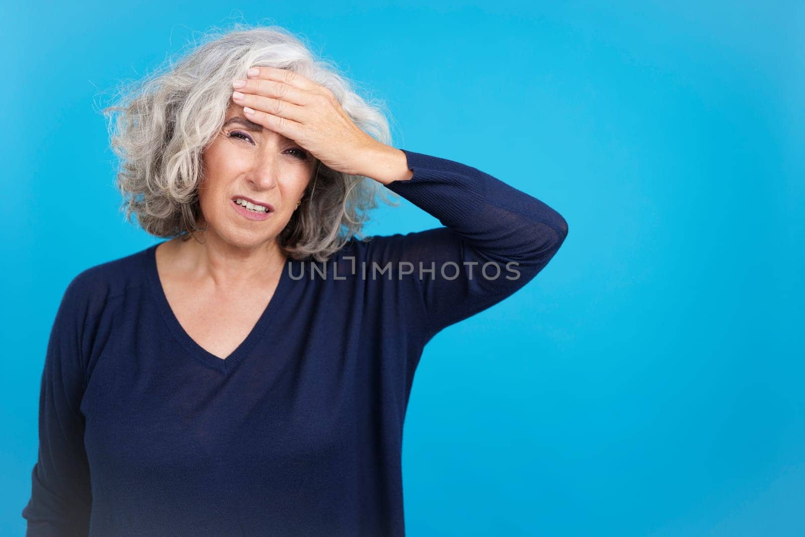Studio portrait with blue background of a mature woman with a headache touching her forehead