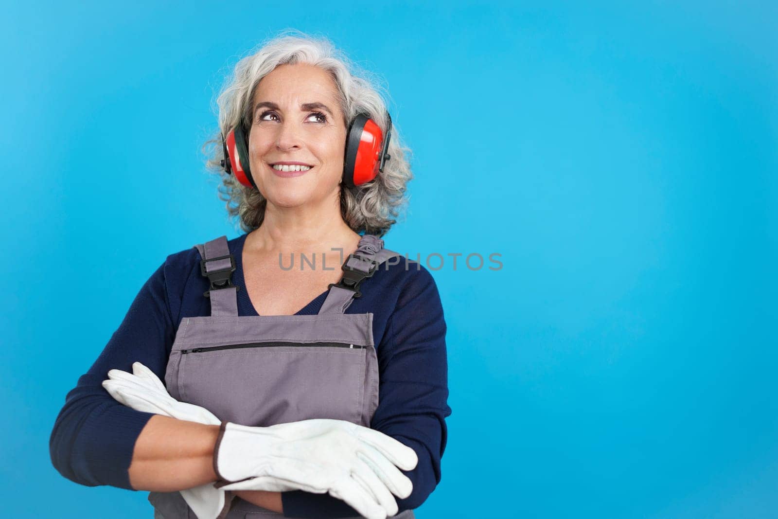 Studio portrait with blue background of a dreamy mature female carpentry worker with tools and work uniform