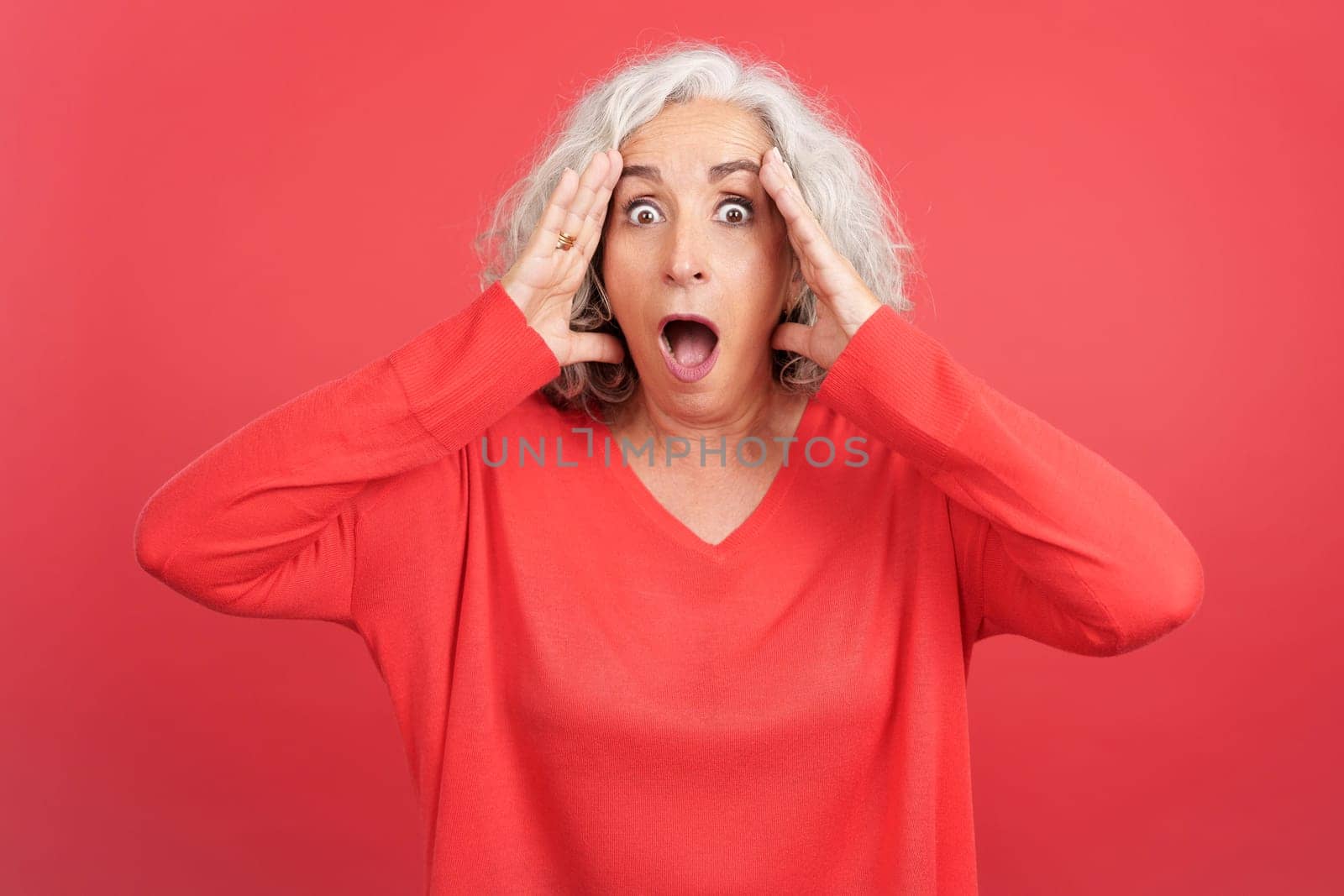 Studio portrait with red background of a mature woman gesturing with a surprised face with the mouth opened