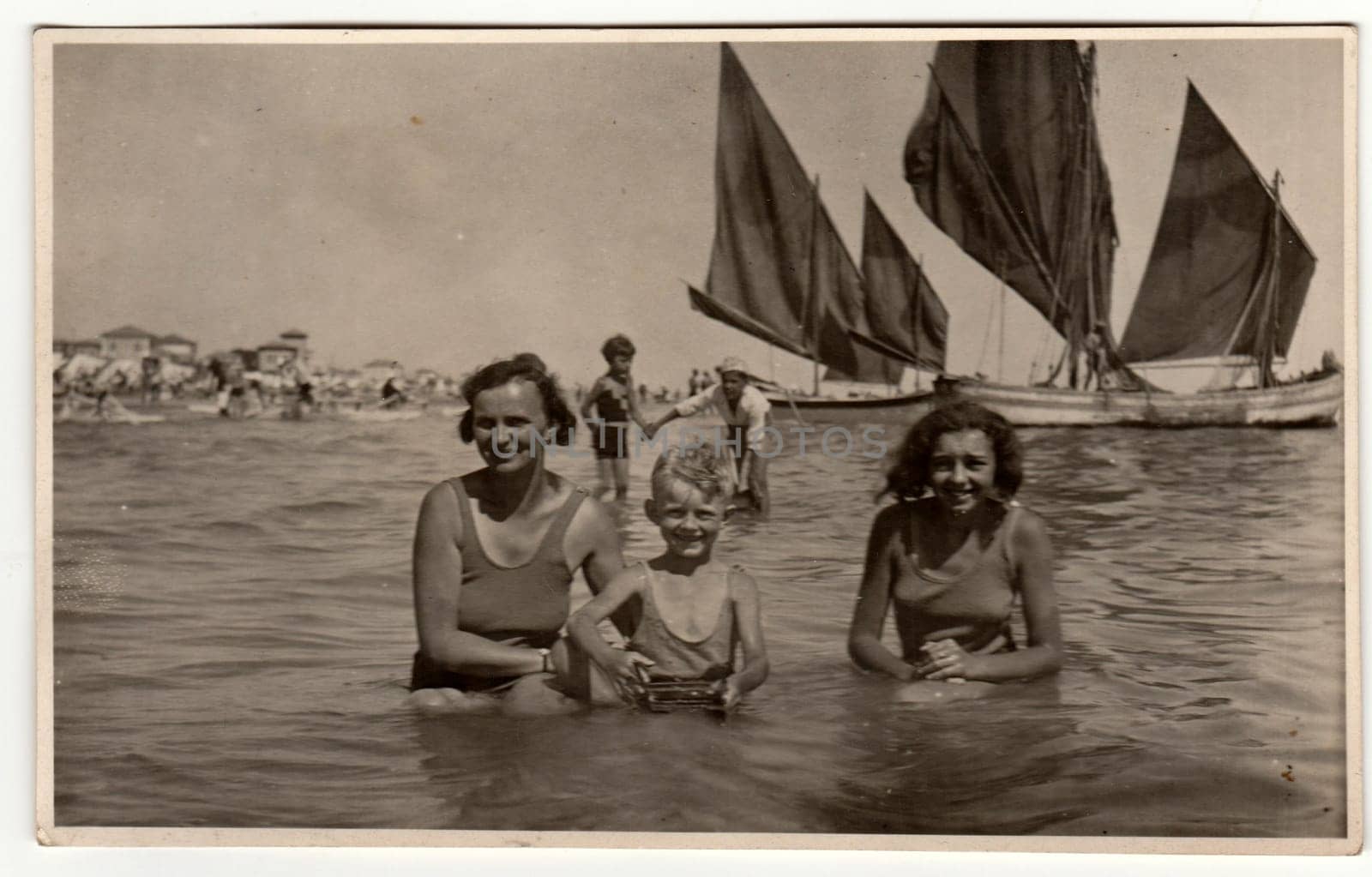 Vintage photo shows family - mother with son and daughter have a swimm in the sea. Sailing boats are on the background. Vacation theme. Retro black and white photography. by roman_nerud