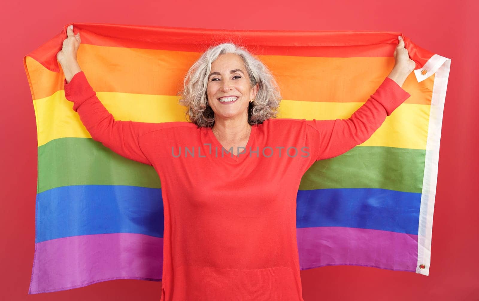 Studio portrait with red background of a Happy woman waving a lgbt rainbow flag