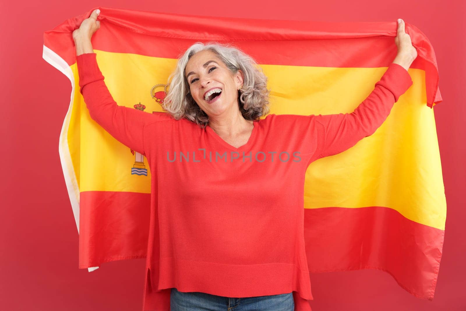 Studio portrait with red background of a happy mature woman raising a spanish national flag