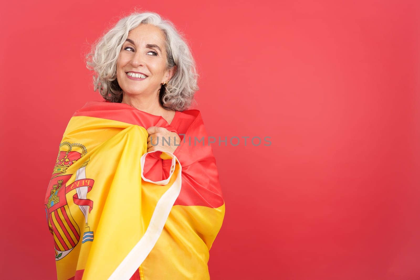 Studio portrait with red background of a happy woman wrapping with a spanish national flag