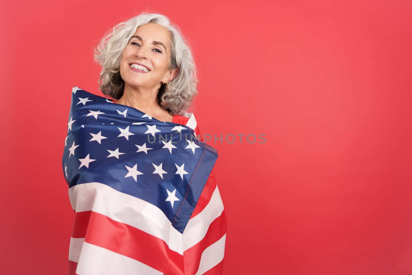 Studio portrait with red background of a smiley woman wrapping with a north america national flag