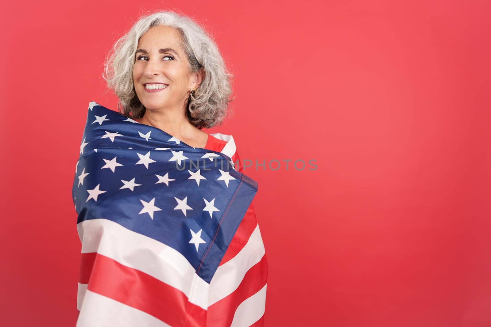 Studio portrait with red background of a happy woman wrapping with a north america national flag
