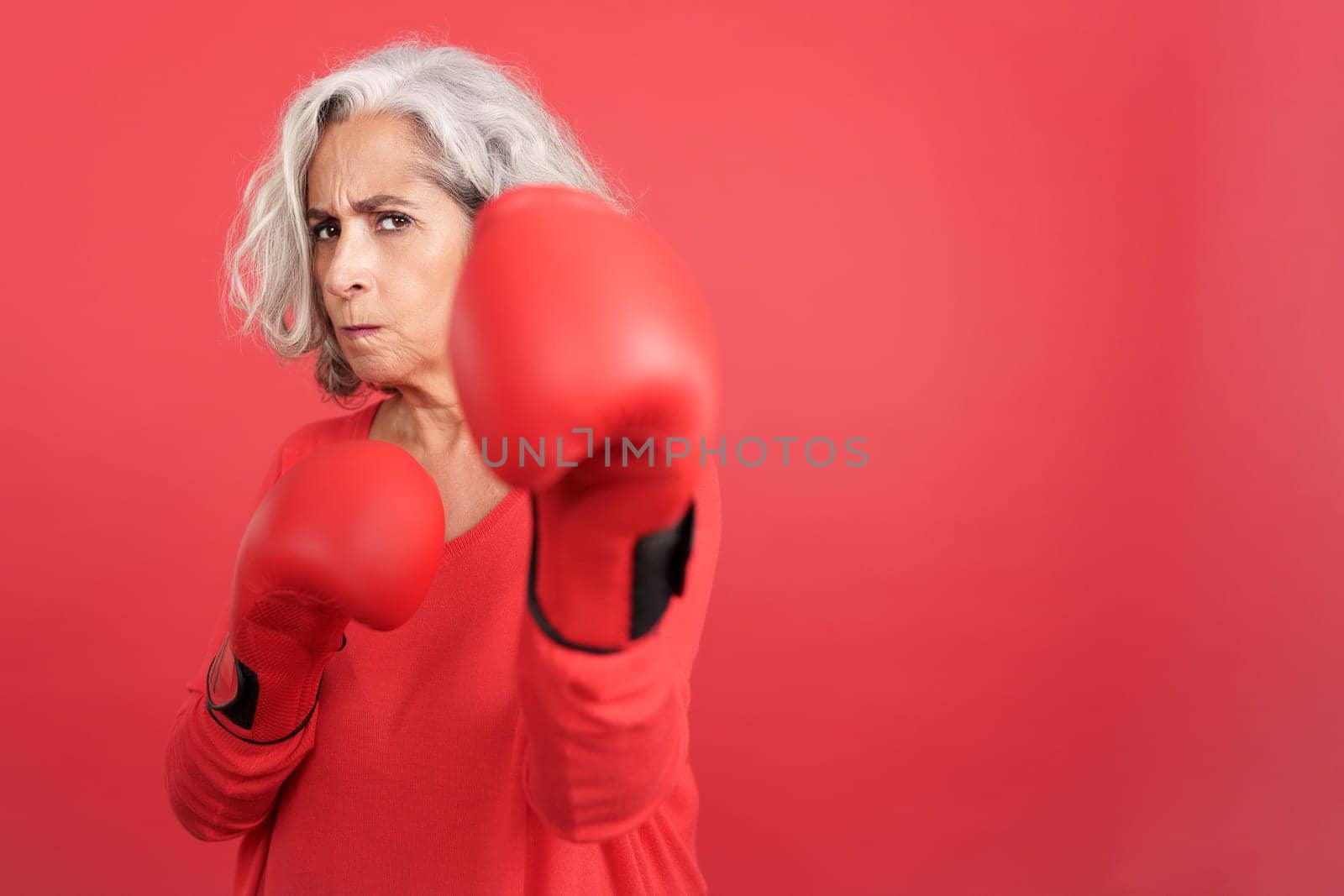 Studio portrait with red background of a mature woman in fighting pose wearing boxing gloves