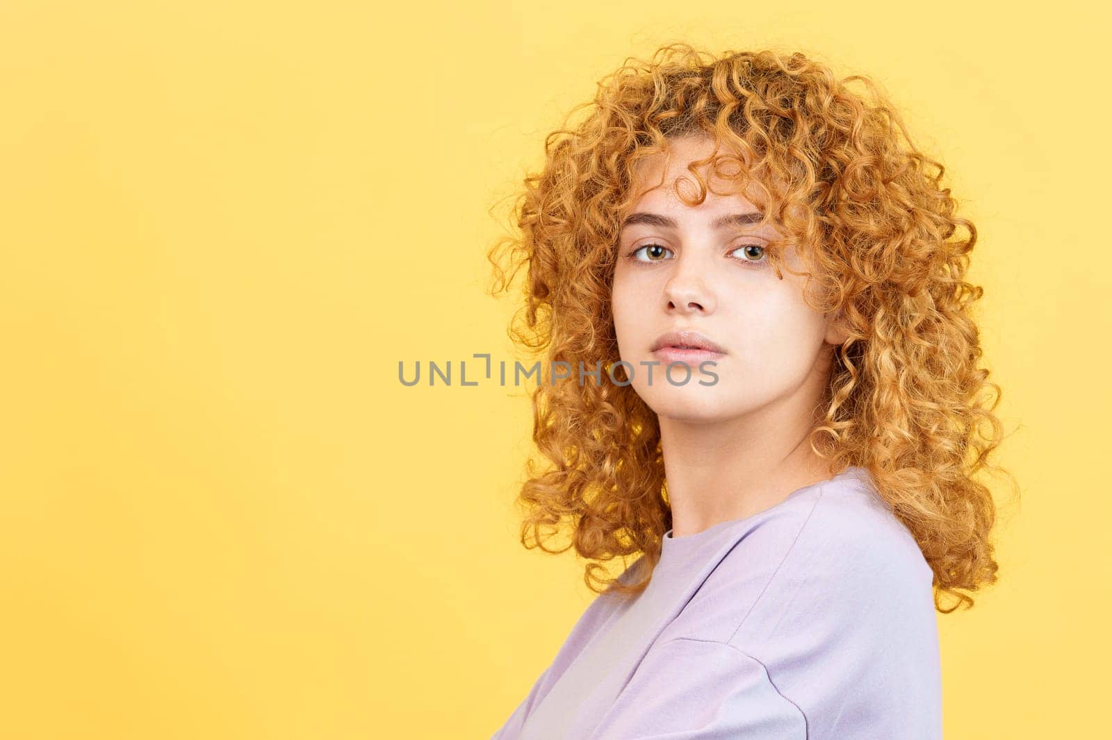 Studio image with yellow background of a beauty woman with curly hair turning to look at the camera