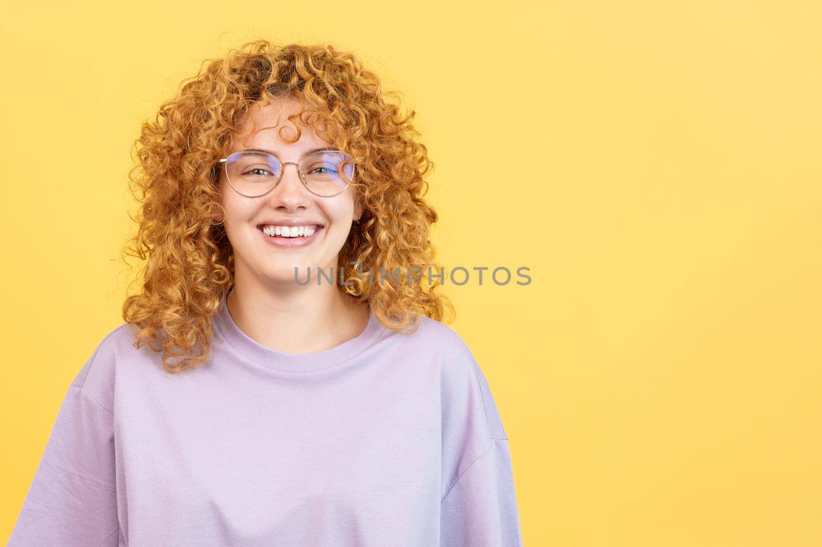 Studio image with yellow background of a happy woman with curly hair with eyeglasses looking at the camera