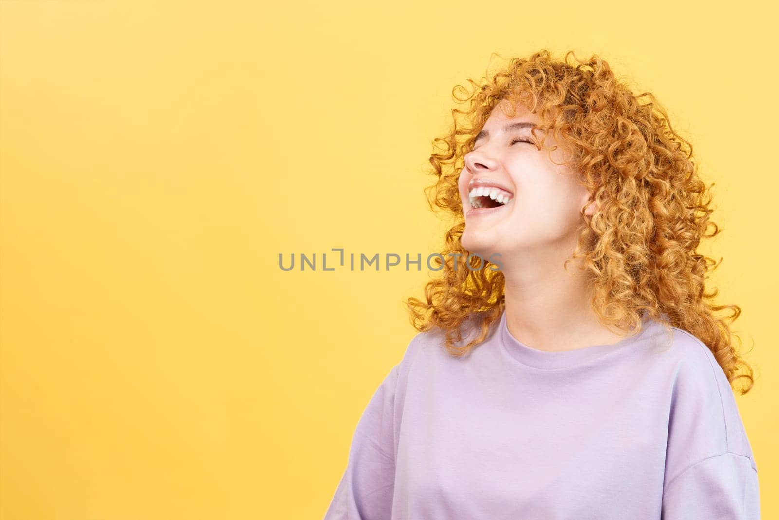 Studio image with yellow background of the profile of a beuty woman with curly hair and casual clothes laughing