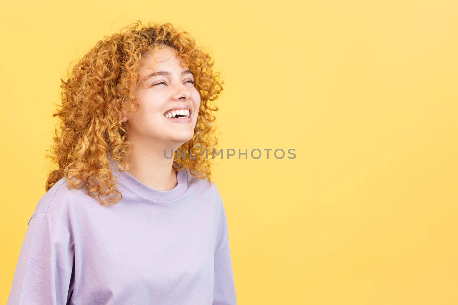 Studio image with yellow background of the profile of a happy woman with curly hair standing