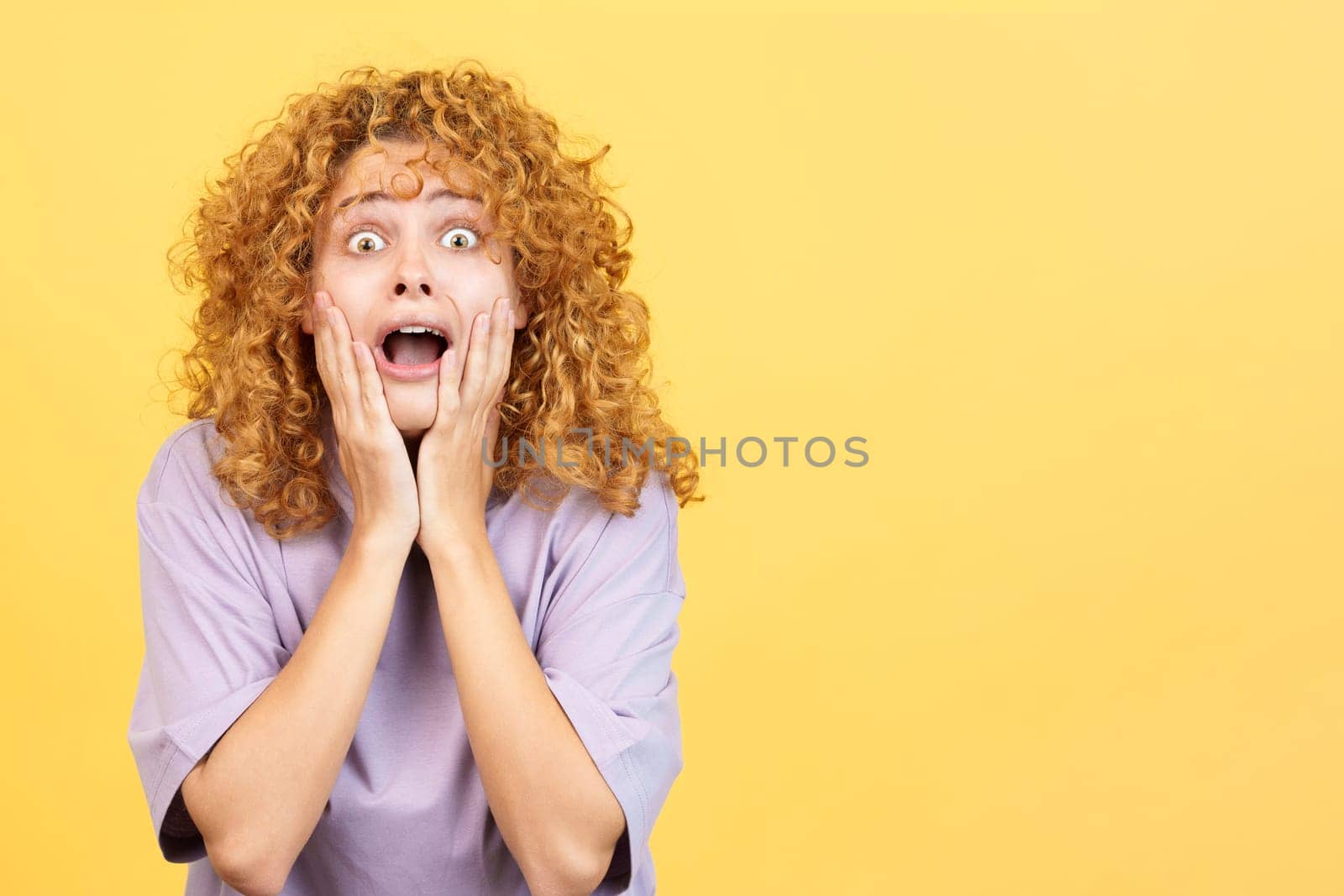 Studio image with yellow background of a beauty woman with curly hair gesturing with the hands on the face expressing dismay