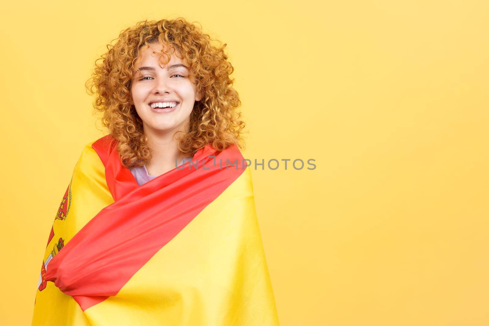 Studio image with yellow background of a beauty woman smiling at camera while wrapping with a spanish national flag