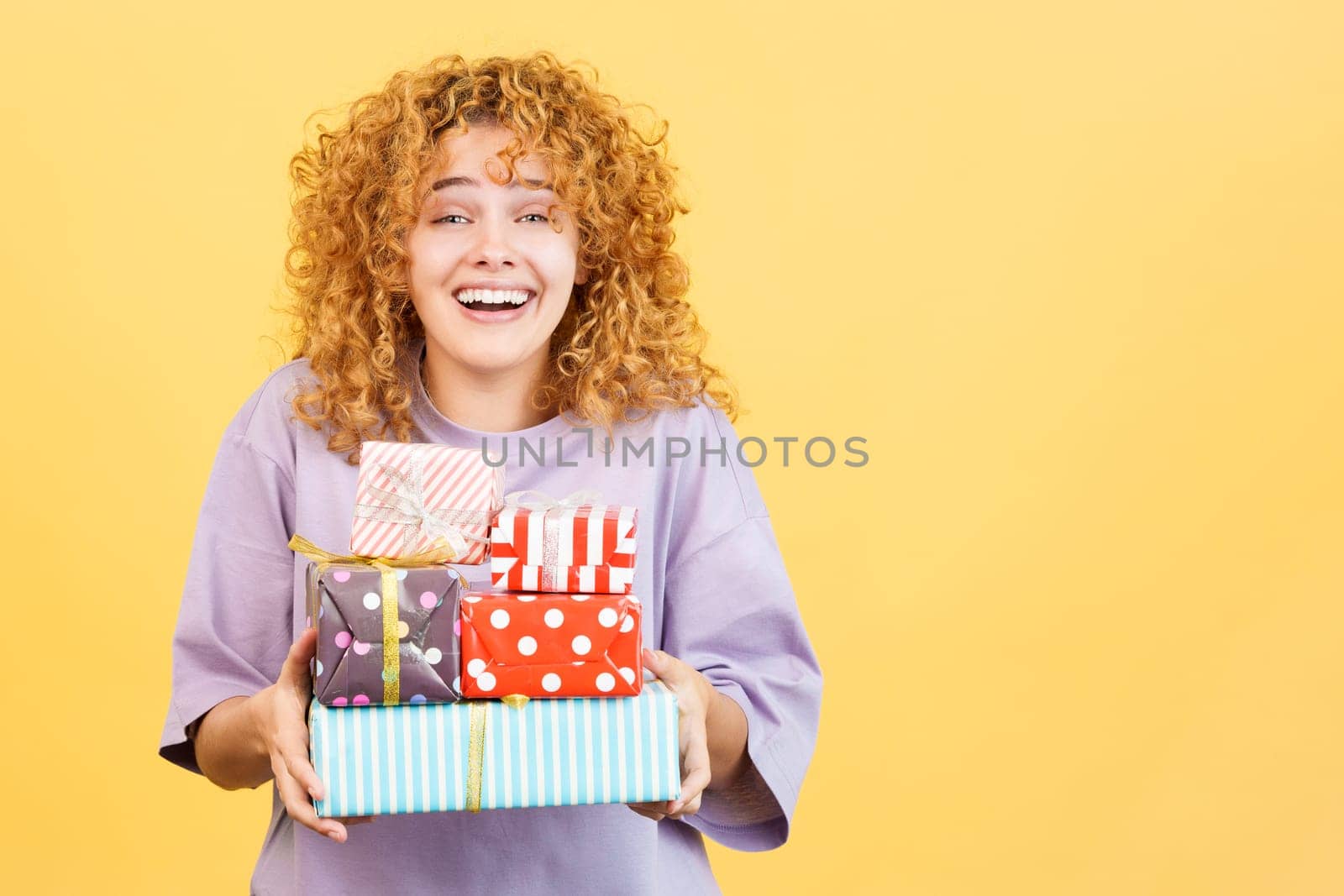 Studio image with yellow background of a emotional young woman smiling at the camera while receiving many gifts