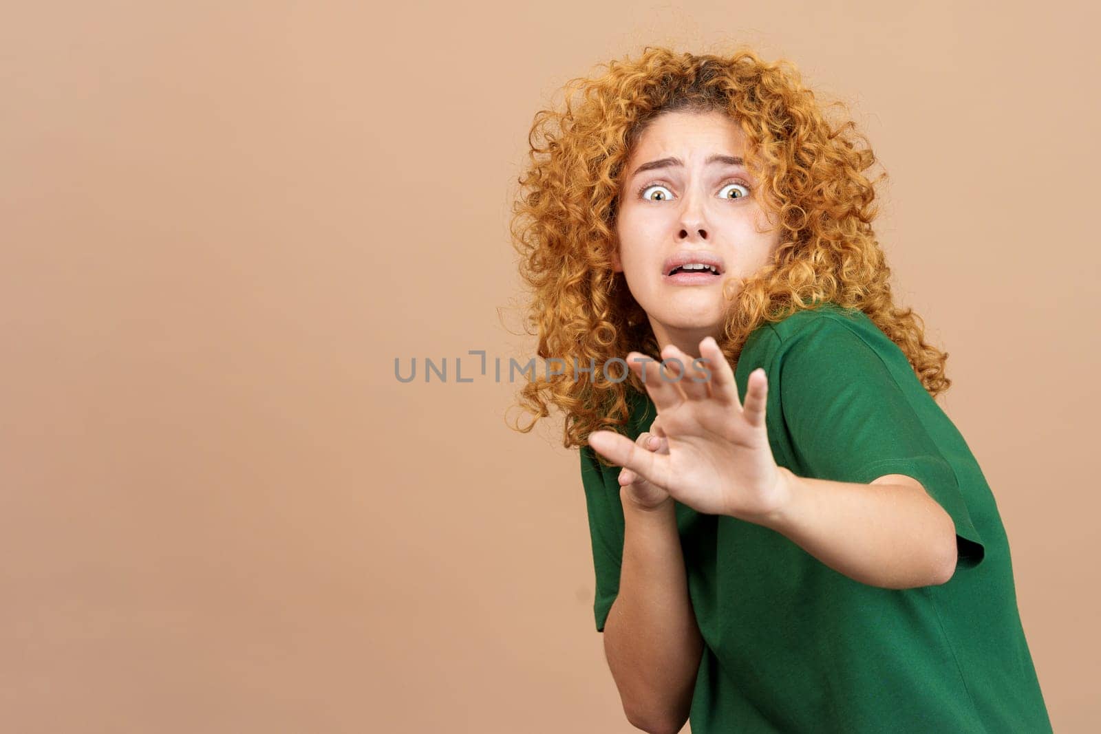 Studio image of a young woman with curly hair gesturing with her hands in fear