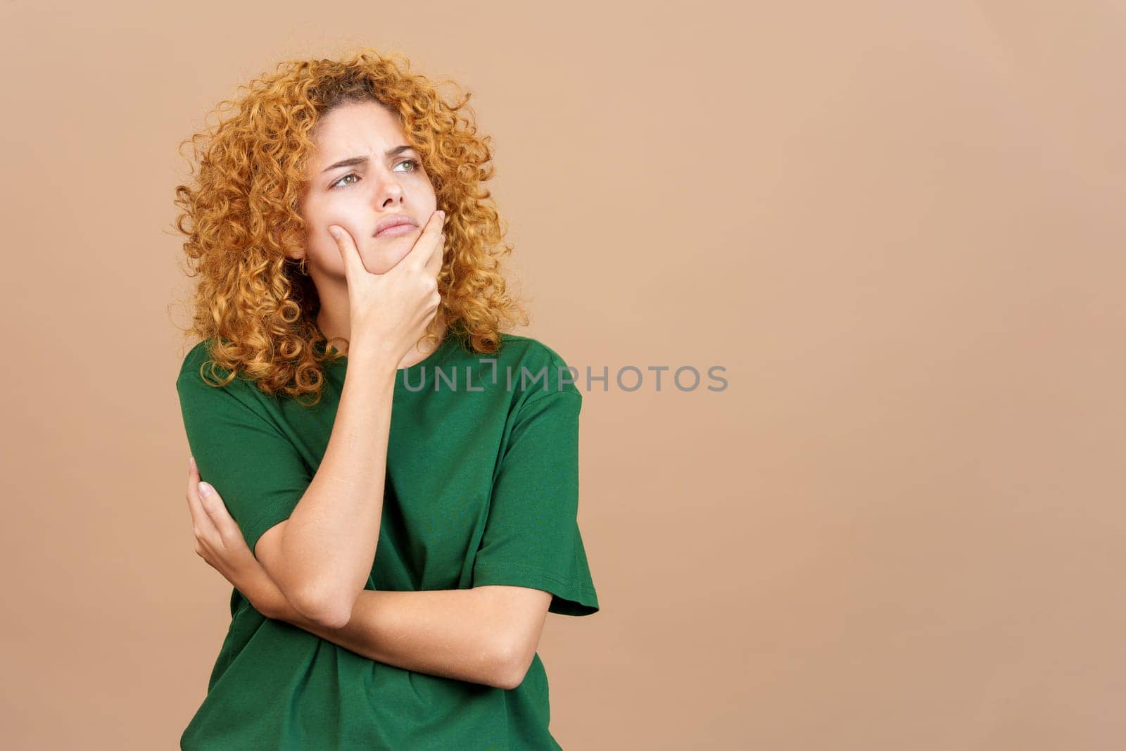 Studio image of a young woman with curly hair gesturing and looking up with doubtful expression