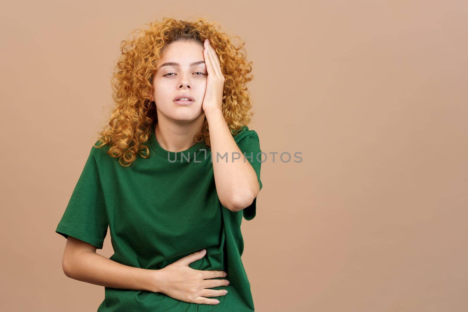 Studio image of a young woman with hand on forehead expressing headache and stomachache