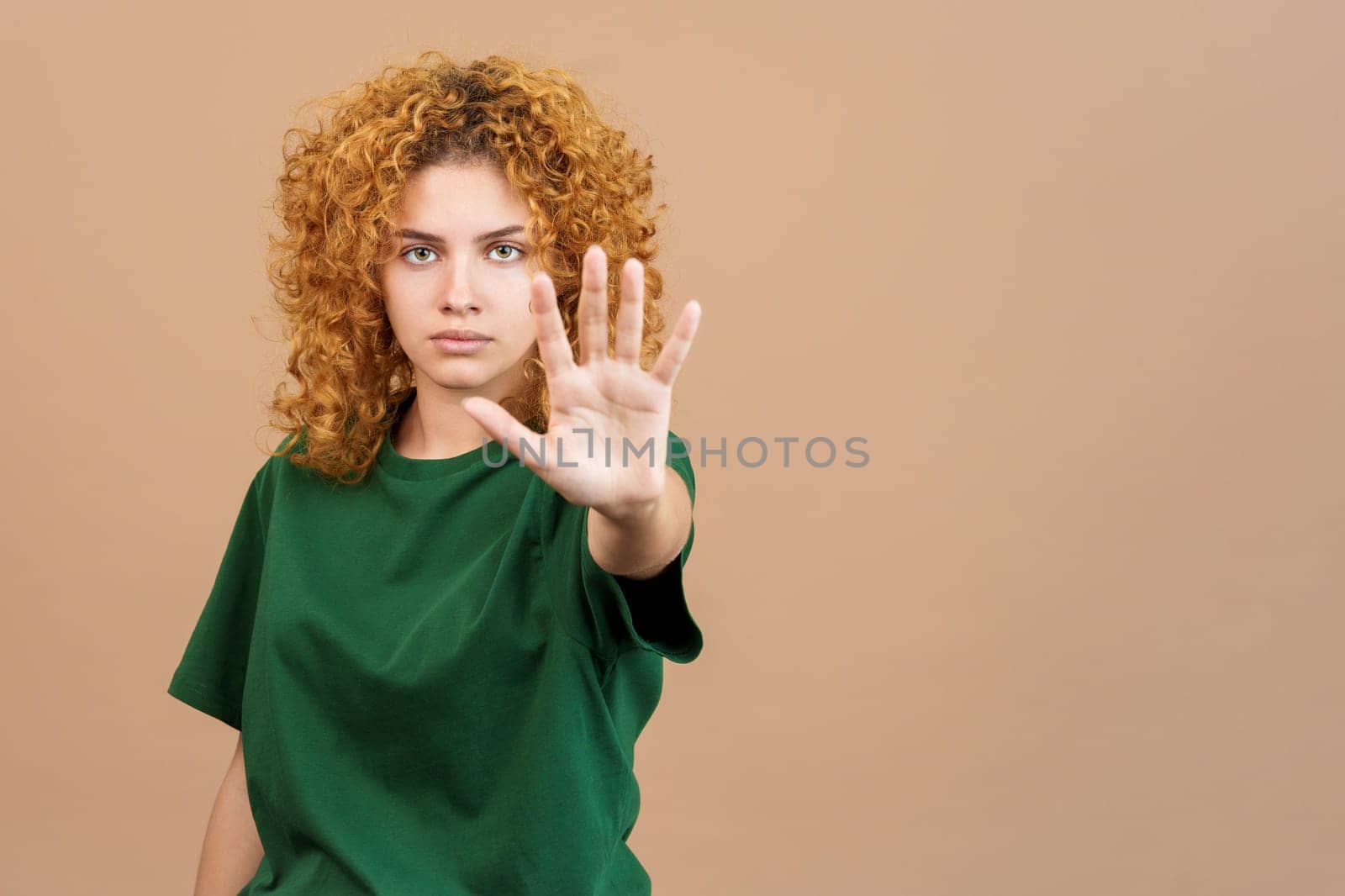 Studio image of a serious young woman with curly hair gesturing with her hand prohibition