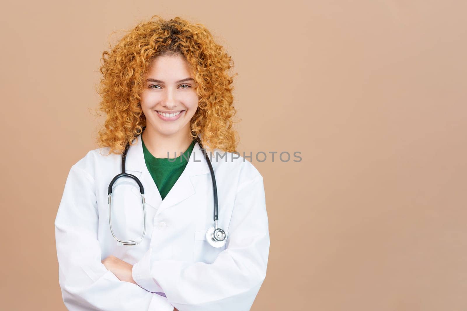 Studio image of a female young doctor with curly hair smiling at camera with the arms crossed