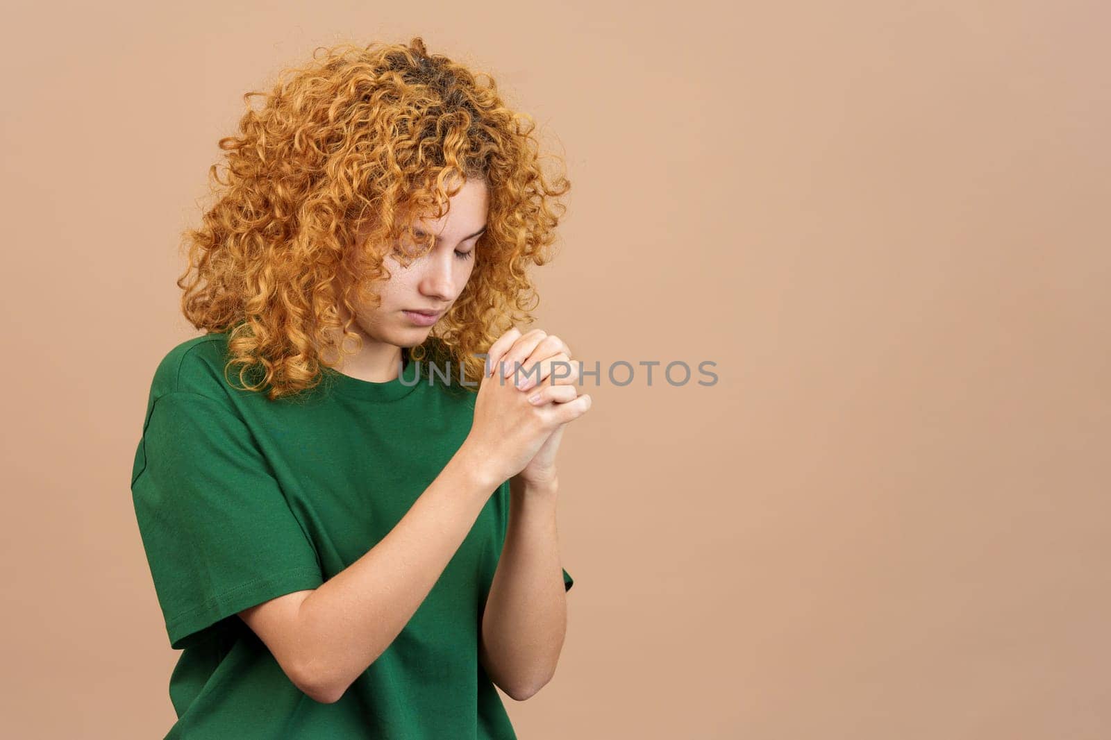 Studio image of a young woman with curly hair praying with folded hands and closed eyes