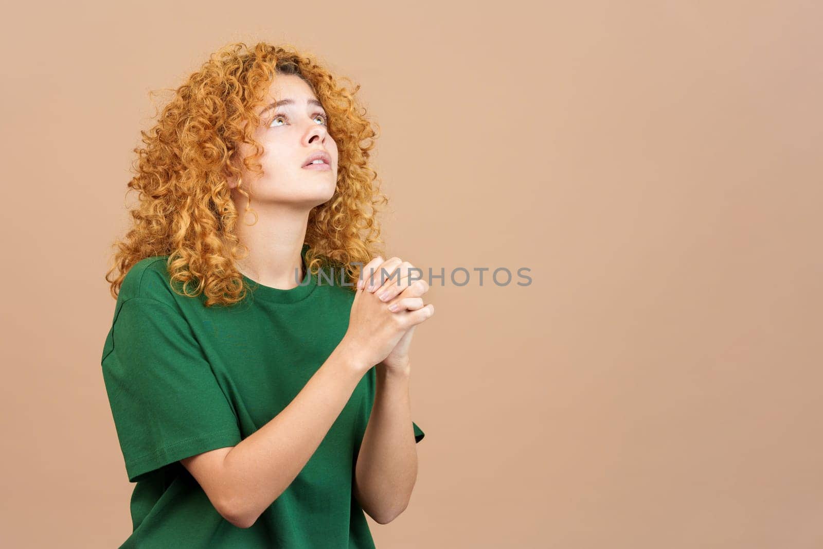 Studio image of a woman with curly hair looking up while praying with folded hands