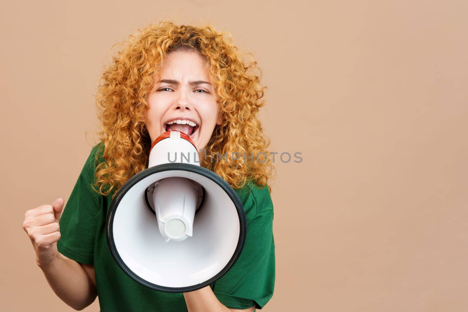 Studio image of a woman with curly hair looking at camera and shouting using a loudspeaker
