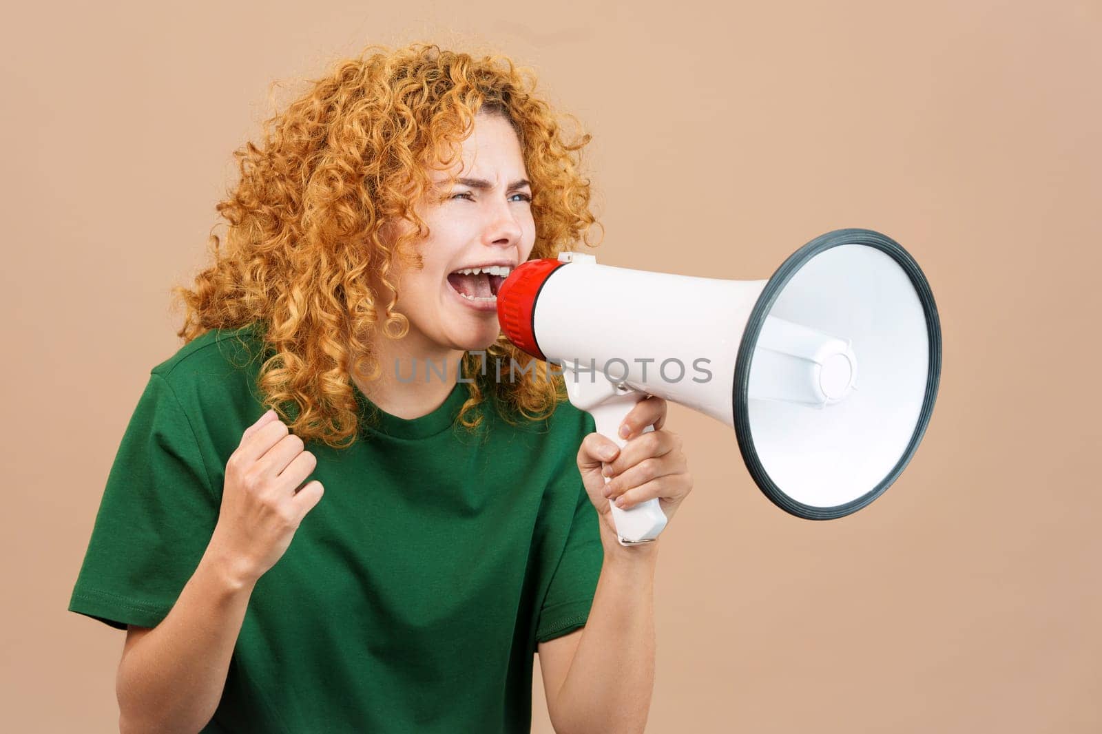 Studio image of an upset woman with curly hair shouting using a loudspeaker