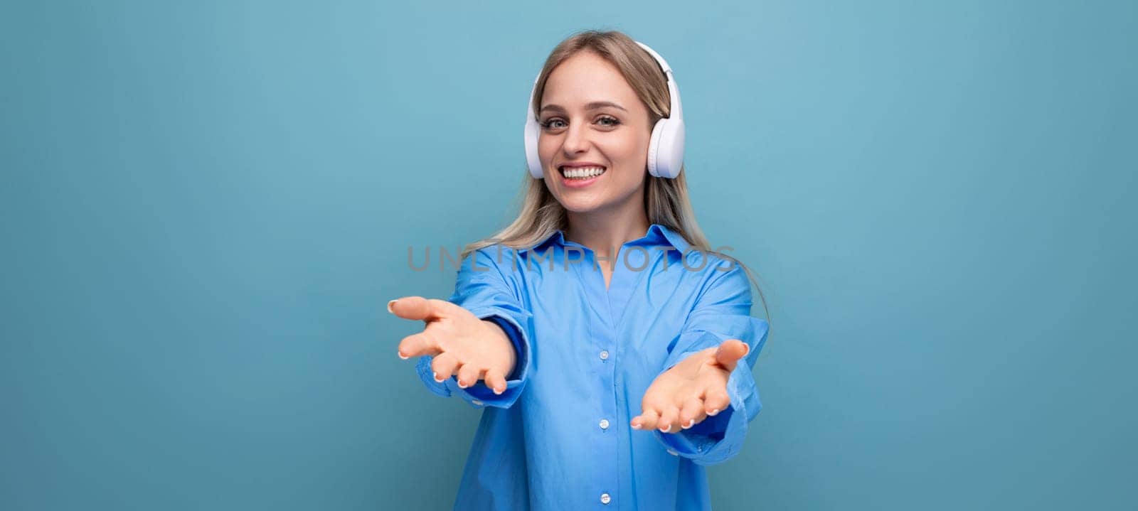 joyful lucky girl in big headphones without a wire stretches out her hands on a blue background with copy space.