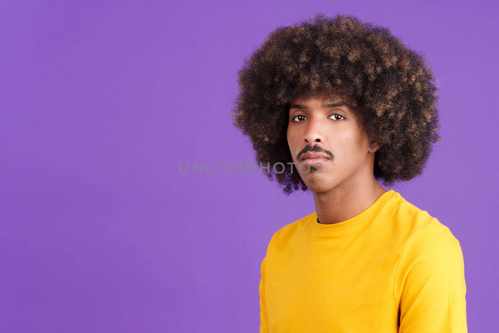 Serious african with curly hair and casual clothing man looking at camera in studio