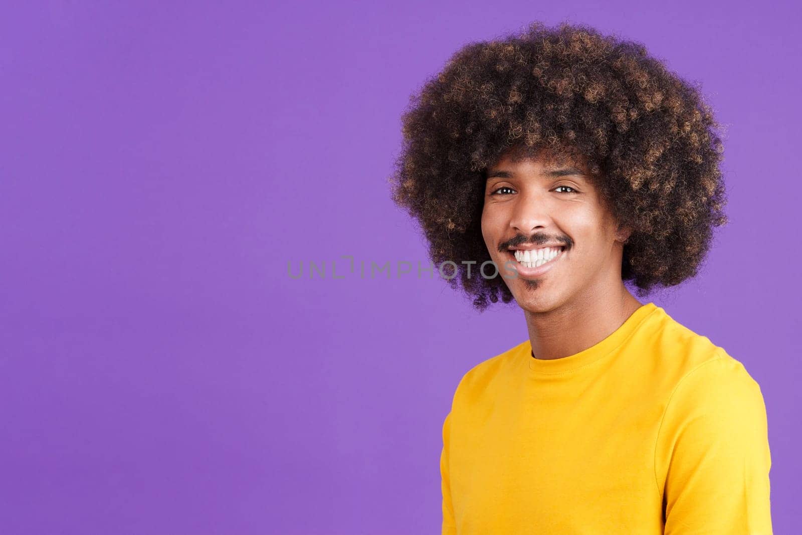 Cool african man with curly hair smiling while looking at camera in studio