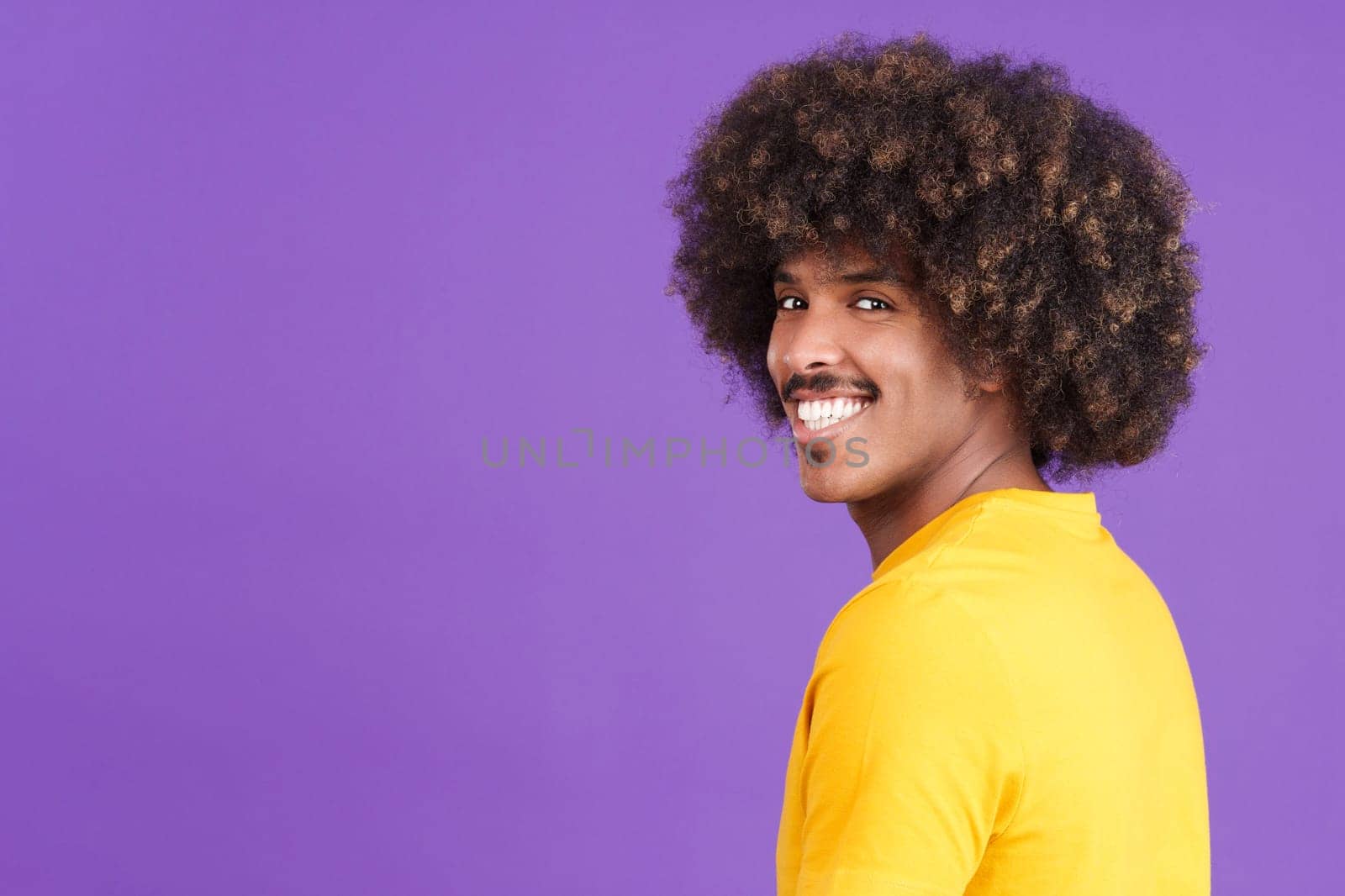 Happy african man with curly hair and casual clothing turning to smile at the camera in studio