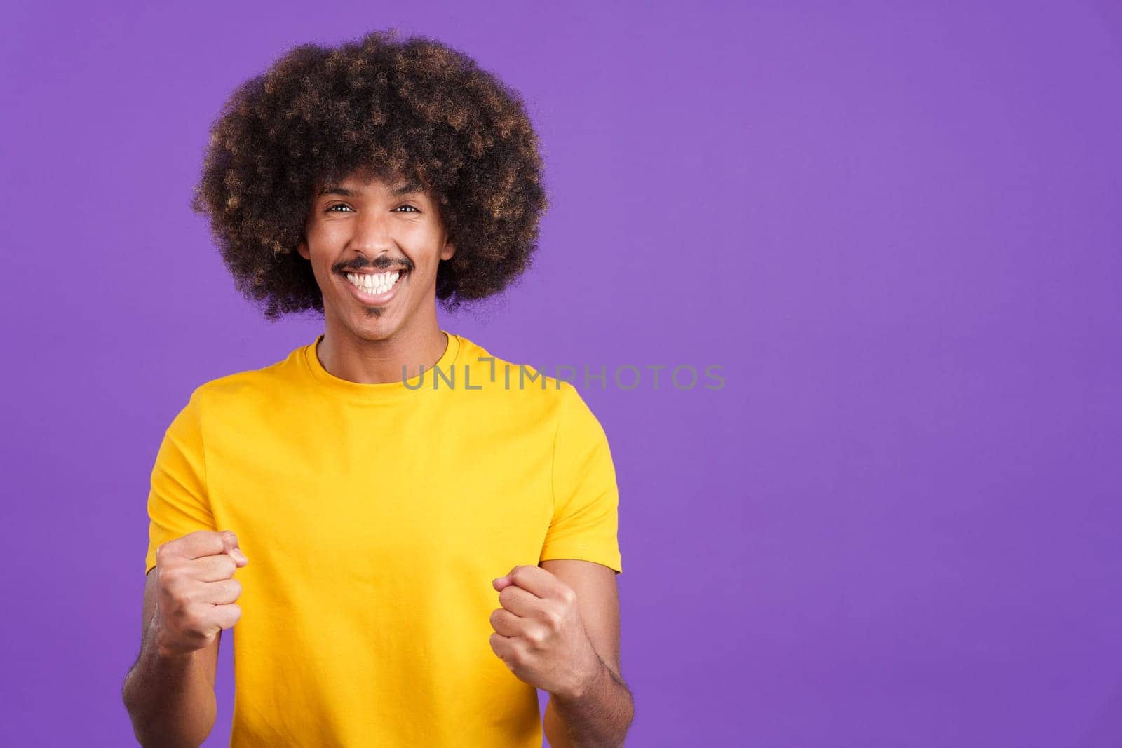Happy african man looking at the camera and celebrating raising the fists in studio