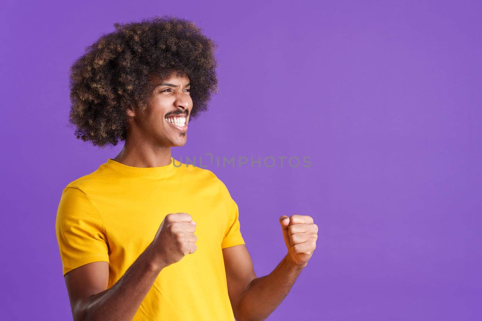 Happy african man with curly hair celebrating raising the fists in studio